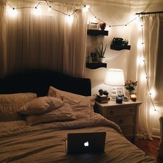 a laptop computer sitting on top of a bed in a bedroom with lights strung around the headboard