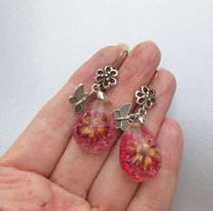 "This very pretty pair of pierced stiver-tone earrings have large oval clear plastic dangles with pink dried flowers embossed inside.  They have from pierced ear wires with have flowers plus little dangling butterflies.  They measure 2\" long and are brand new in mint condition.    FREE SHIPPING within the USA and they will arrive gift boxed!    0040" Pink Dried Flowers, Pierced Ear, Flower Butterfly, Artisan Earrings, Dried Flower, Clear Plastic, Ear Wires, Ear Piercings, Dried Flowers