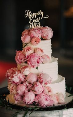 a three tiered cake with pink flowers on the side and a sign that says happily married