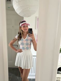 a woman taking a selfie in front of a mirror wearing a white dress and pink hat