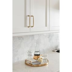 a marble counter top with two glasses and a bottle on it in front of white cabinets