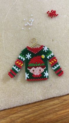 a christmas sweater ornament is hanging on a table next to beads and thread