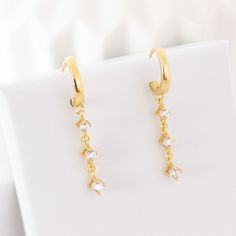 These huggie earrings are made from 18 karat gold-plated sterling silver and consist of a smooth, plain hoop with a hinged closure, and a row of 3 tiny zirconia stones dangling from their lower edge. Classy yet versatile, these huggies will elevate your everyday outfits or will add the perfect finishing touch to your next party outfit.  Also available in silver:  https://www.etsy.com/listing/1034046220/dangle-huggie-earrings-sterling-silver 🎁 Packaging: Beautifully packed in a box, ready for gifting. 🏷️ This product is made of sterling silver -- easily recognizable by its '925' stamp of authenticity. It is also hypoallergenic, making it suitable for people with sensitive or irritable skin. We recommend avoiding perfume, deodorant or other chemicals. Details: ✅ Material: 925 sterling silv Minimalist Gold Plated Drop Huggie Earrings, Minimalist Yellow Gold Dangle Huggie Earrings, Classic Gold Plated Dangle Huggie Earrings, Hypoallergenic Yellow Gold Huggie Dangle Earrings, Gold Dangle Huggie Earrings With Lever Back, Silver Packaging, Huggie Earrings Gold, Hoops Earrings, Huggie Earrings