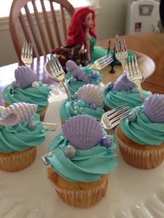 cupcakes with blue frosting and sea shells on them are sitting on a table