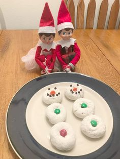 two elfs sitting next to each other near a plate with snow covered donuts on it