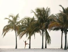 a person standing in front of palm trees on the beach with their arms up and legs crossed