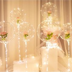 three clear balloons with roses in them on top of a white box and some lights