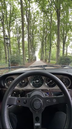 the dashboard of a car driving down a road in front of some trees and bushes