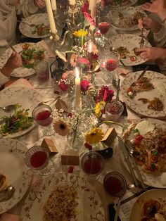 a group of people sitting around a table with food and candles in the middle of it