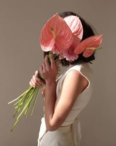 a woman holding flowers in her hands and wearing a white dress with pink flowers on it