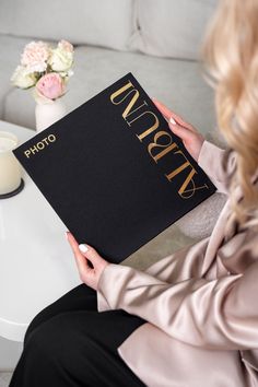 a woman sitting on a couch holding up a black book with gold lettering that reads photography