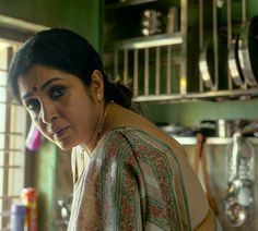 a woman standing in a kitchen looking at something on the counter and holding a knife