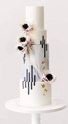 a three tiered cake with white and black designs on it, topped with flowers