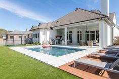 a house with a pool and deck chairs in the front yard, surrounded by lush green grass