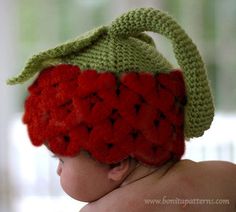 a baby wearing a crocheted strawberry hat with leaves on it's back