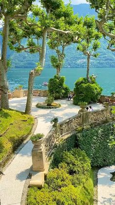 an outdoor garden with statues and trees in the foreground, overlooking water and mountains