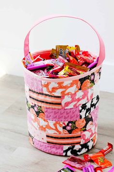 a pink basket filled with candy and candies on top of a wooden floor next to a white wall