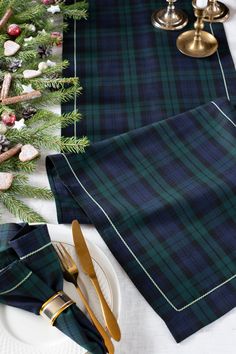 the table is set with plaid napkins and gold utensils for christmas dinner