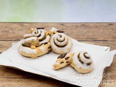 three doughnuts with chocolate and white icing are on a paper towel sitting on a wooden table