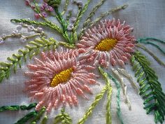 some pink and yellow flowers are on a white table cloth with green thread work in the middle