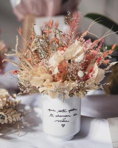 a white vase filled with lots of flowers on top of a cloth covered tablecloth