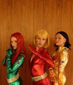 three women dressed in costumes standing next to each other on a wooden floor with wood paneling behind them