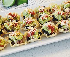 small appetizers are lined up on a white platter with limes in the background