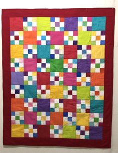 a colorful quilt hanging on the wall in front of a white wall with a red frame