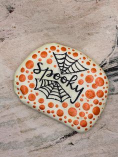 a decorated rock sitting on top of a sandy beach covered in orange and black dots