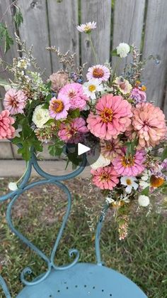 a bouquet of flowers sitting on top of a blue chair in front of a fence