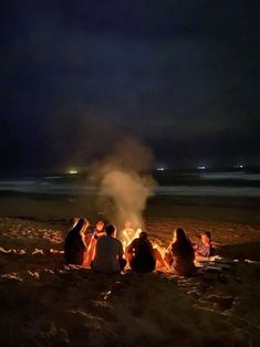 people sitting around a campfire on the beach at night