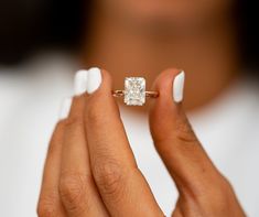 a woman's hand holding an engagement ring with a square diamond in the middle