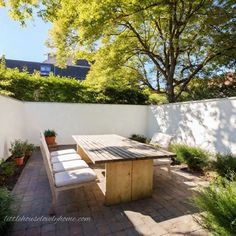 a wooden table sitting on top of a brick patio next to a white fence and trees