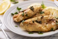 two pieces of chicken on a plate with lemons and capers next to it