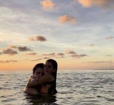 two women are hugging in the water at sunset or dawn, with clouds above them