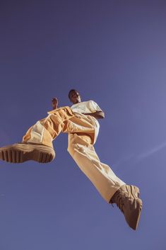 a man flying through the air while wearing yellow pants and brown boots with his feet in the air