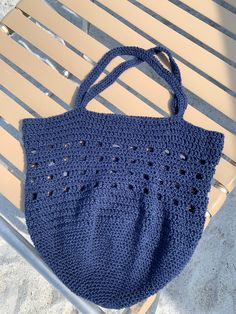 a blue crocheted bag sitting on top of a wooden bench next to a plastic chair