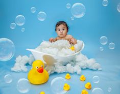 a baby sitting in a bathtub surrounded by soap bubbles and rubber ducky toys