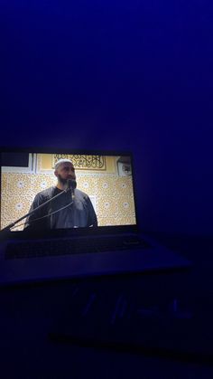 a laptop computer sitting on top of a desk with a man talking into a microphone