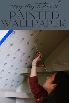 a woman is working on the ceiling with paint and wallpaper in front of her