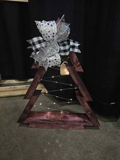 a christmas tree made out of wood with lights and bows on the top, sitting in front of a black background