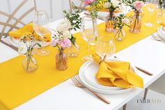 the table is set with yellow napkins, white plates and flowers in vases