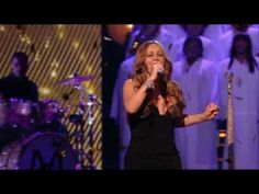 a woman singing into a microphone in front of an audience with choirs behind her