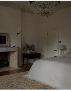 a bedroom with a chandelier hanging from the ceiling and a bed in front of a fireplace