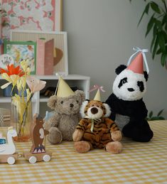 three stuffed animals are sitting on a table with party hats and decorations around them,