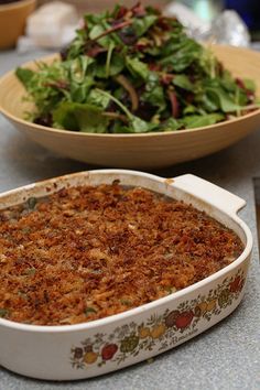 a casserole dish filled with food next to a bowl of salad on a table