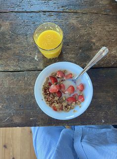 a bowl of cereal with yogurt and strawberries next to a glass of orange juice