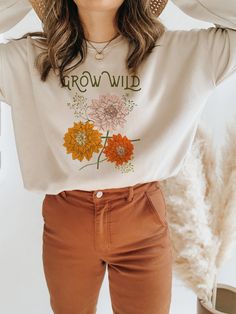 a woman wearing brown pants and a white t - shirt with flowers on the front