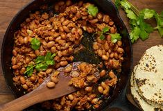 a skillet filled with beans and meat next to tortilla bread on a wooden table