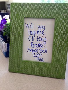 a green frame sitting on top of a counter next to a potted purple flower